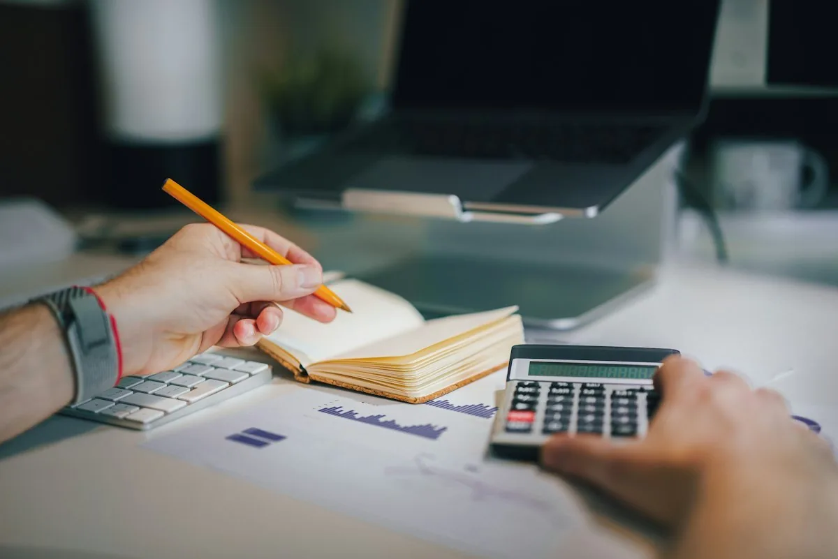Person using a calculator and writing notes beside financial charts
